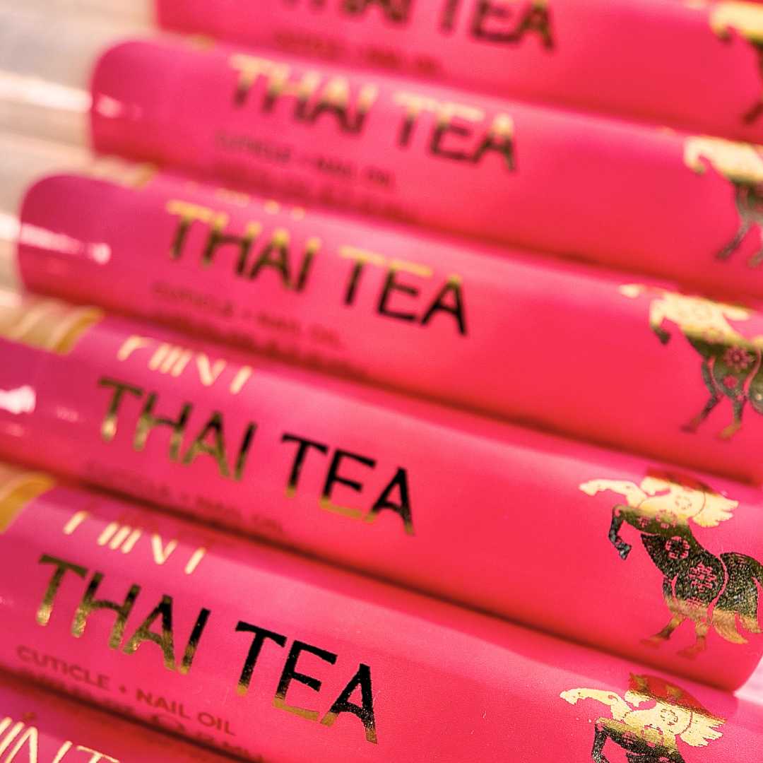 Stack of pink 'THAI TEA' cuticle oil twist pens with decorative labels.