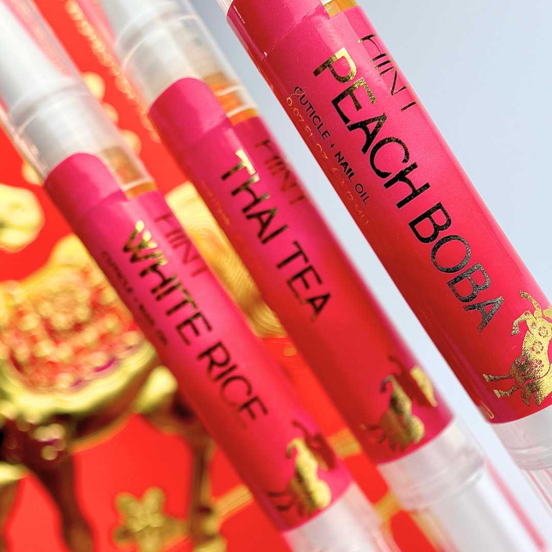 Three tubes of cuticle oil in front of a red envelope background